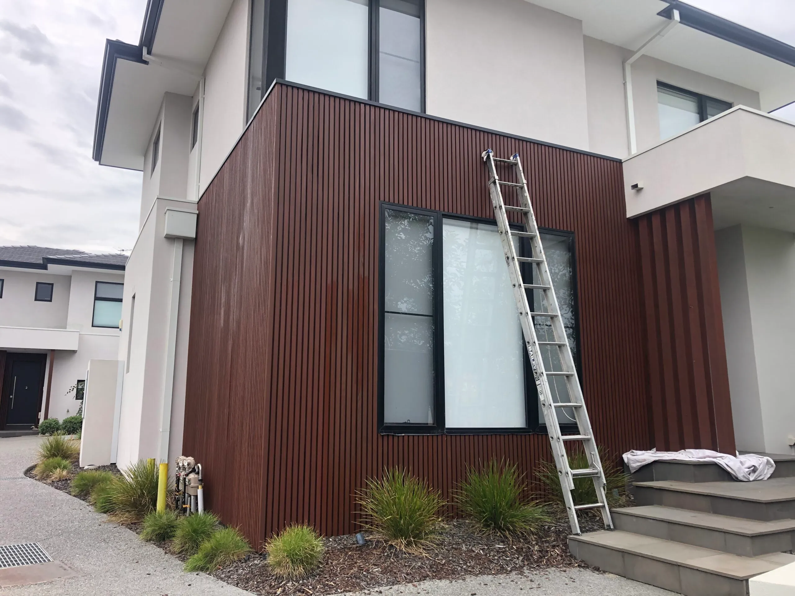 Ladder and drop sheet set up against freshly stained vertical timber cladding on a modern Melbourne townhouse